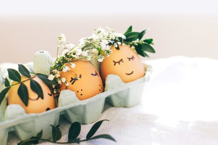 Stylish Easter eggs with cute faces in floral wreath crowns in carton tray